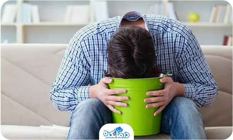 مردی که روی مبل نشسته و در حال استفراغ در یک سطل است