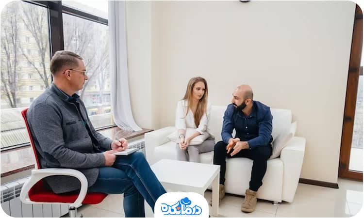 یک پزشک در مطب نشسته و یک خانم و آقا در حال گفتگو هستند.